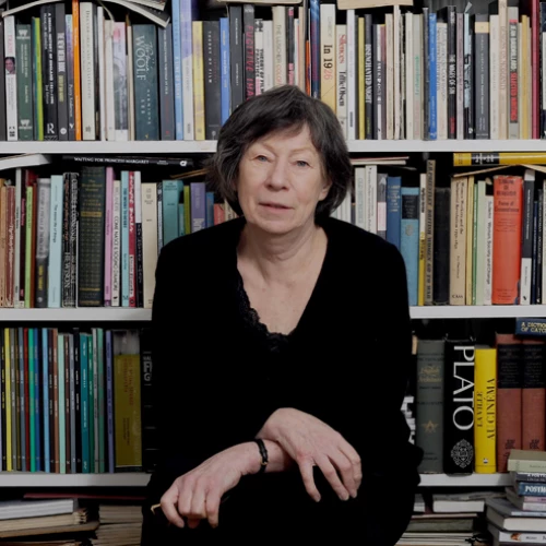 Porträt von Laura Mulvey in schwarzer Kleidung vor einer bunten Bücherwand