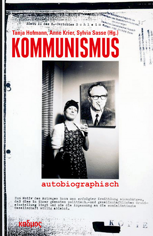 Eine Frau mit Kopftuch und Schürze steht lächelnd vor einem Porträt von Erich Honecker